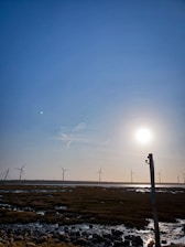 Modern wind turbines spinning on a green field with clear blue sky background.