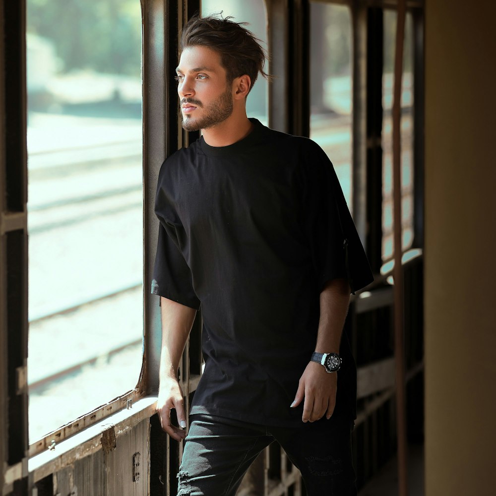 man in black crew neck t-shirt standing near glass window during daytime