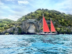 white and red sail boat on blue sea near green and brown mountain under blue and