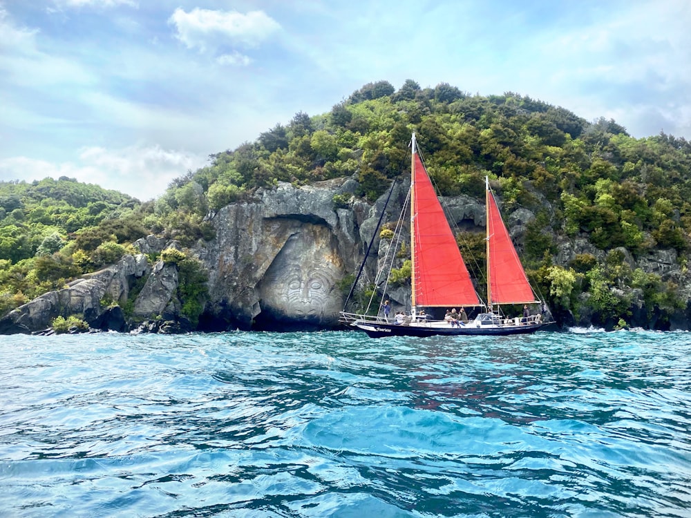 barco a vela branco e vermelho no mar azul perto da montanha verde e marrom sob azul e