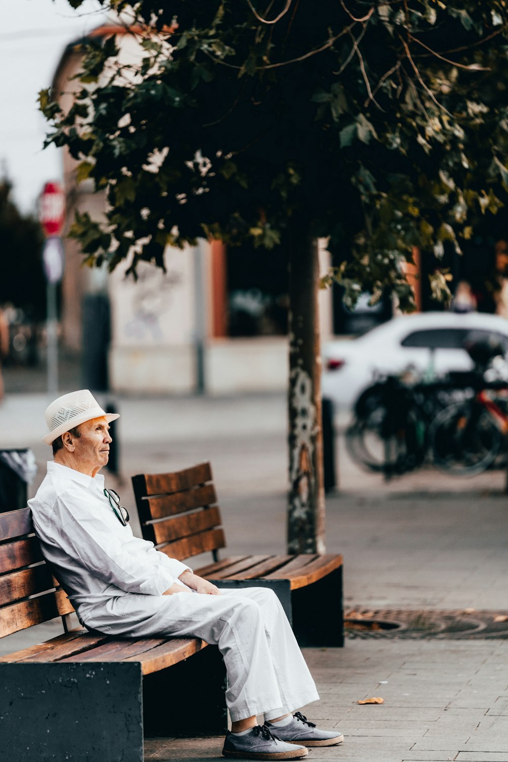 man in white thobe sitting on brown wooden bench during daytime