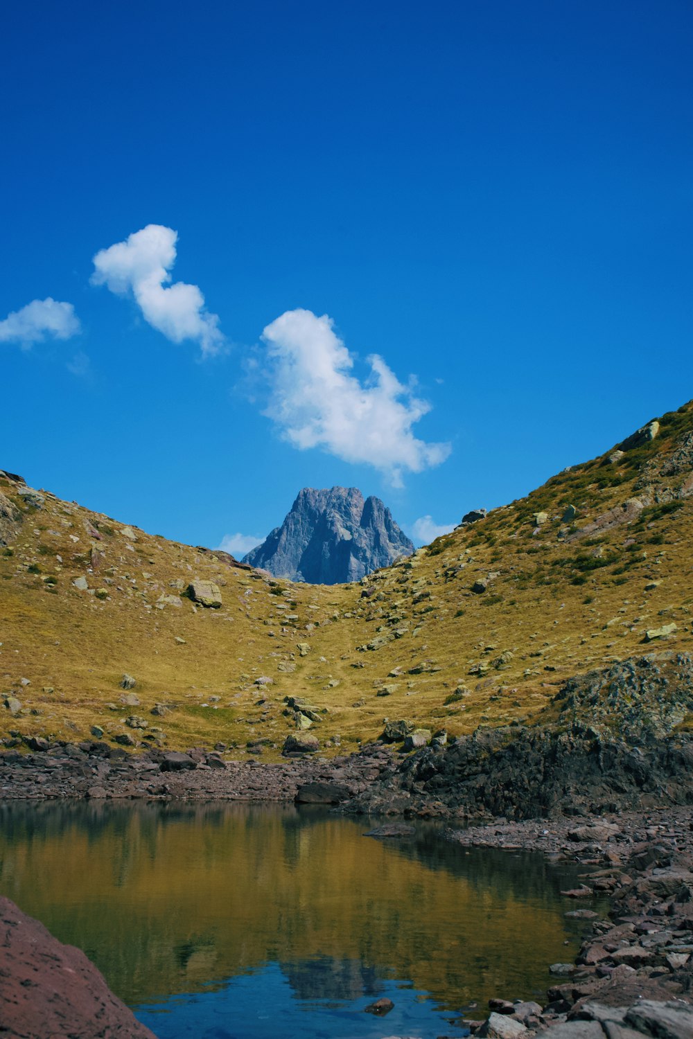 green and brown mountain beside lake under blue sky during daytime