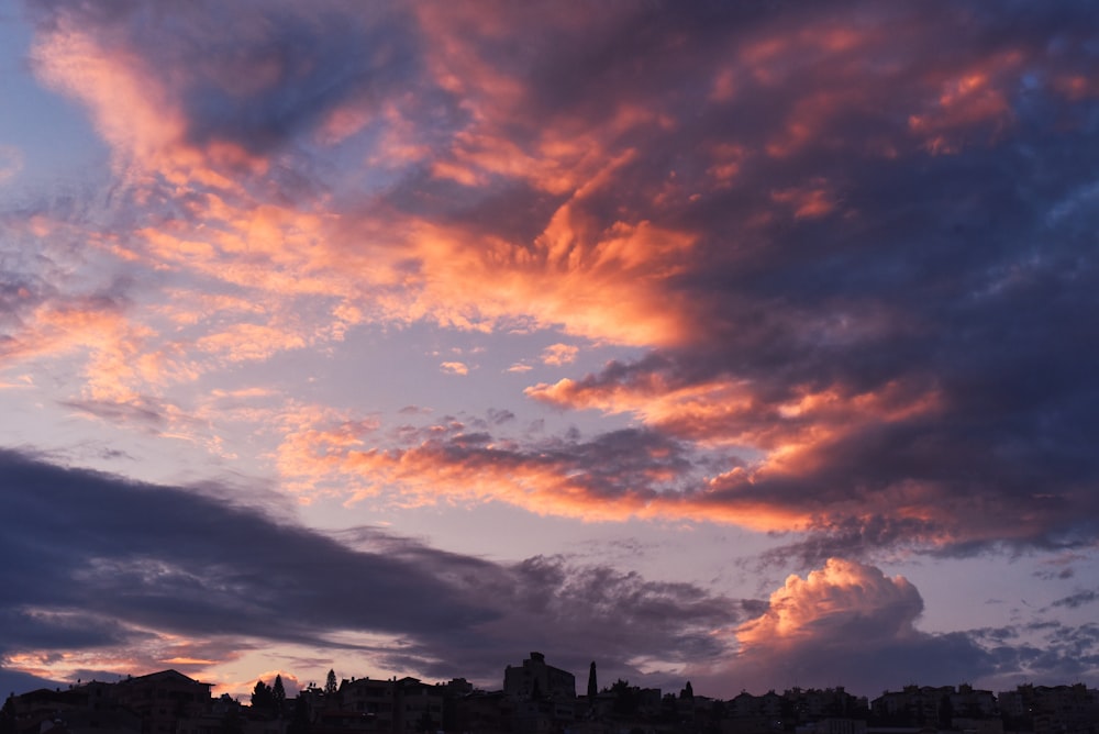 silhouette of buildings under orange and gray clouds