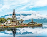 brown and green temple near body of water under blue and white cloudy sky during daytime