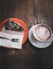 Close-up of a steaming cappuccino beside a plate of freshly baked carrot cake on cream linen.