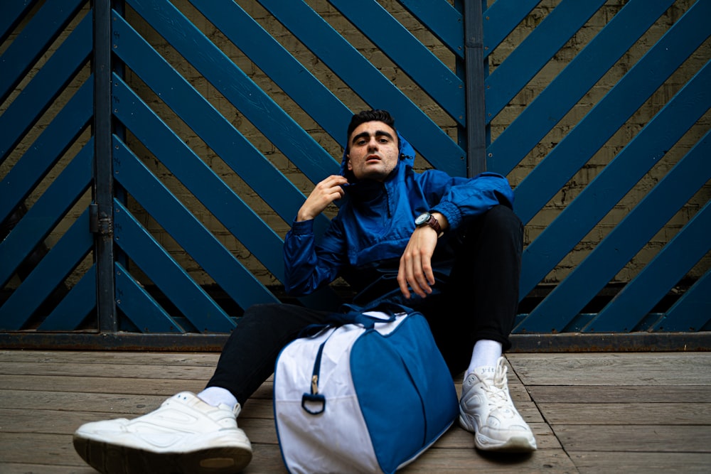 man in blue jacket and black pants sitting on wooden bench