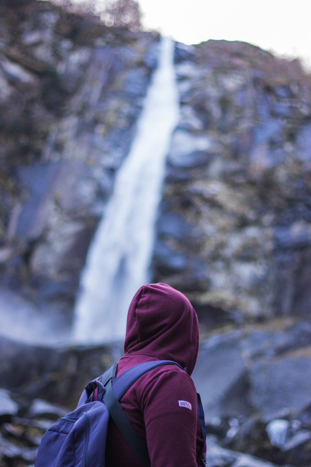 person in red hoodie standing near waterfalls during daytime