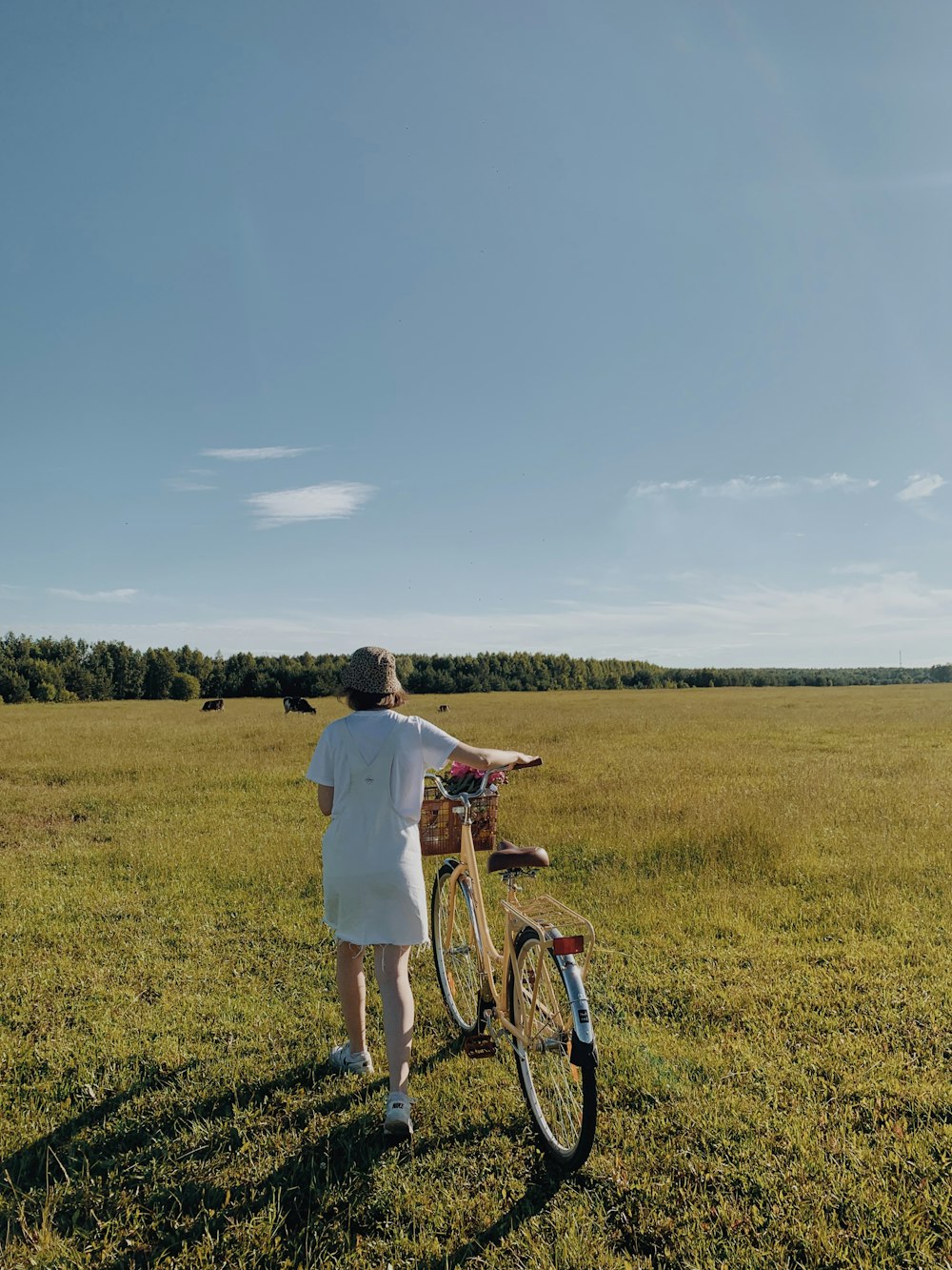 man in white t-shirt and blue denim jeans holding bicycle on green grass field during