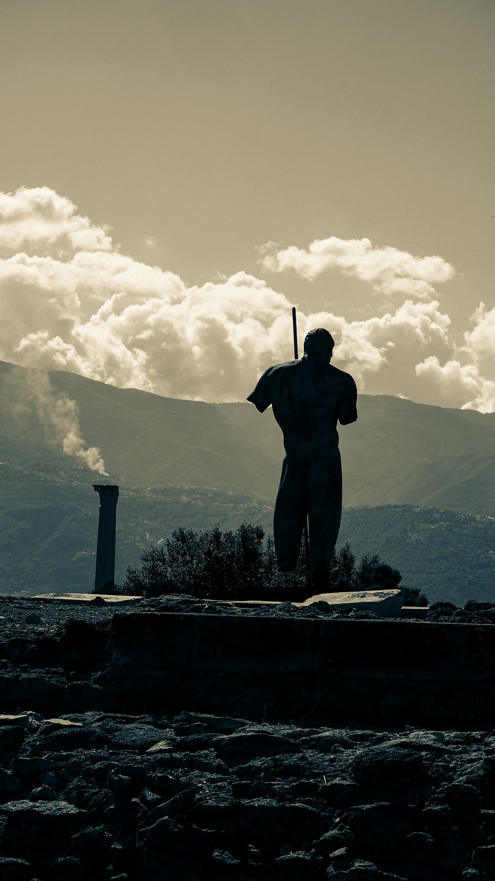 昼間の曇り空の下、山の近くのコンクリートの壁の上に立つ男のシルエット
