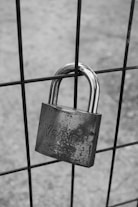 grayscale photo of padlock on metal fence