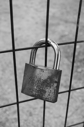 grayscale photo of padlock on metal fence