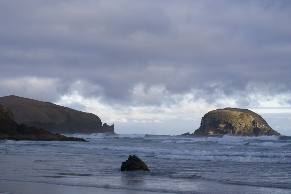 brown rock formation on sea under white clouds during daytime