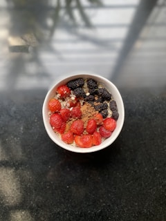 A bowl filled with fresh strawberries and blackberries on a base of oatmeal, sprinkled with cocoa powder and chia seeds, placed on a dark surface with soft, natural lighting.