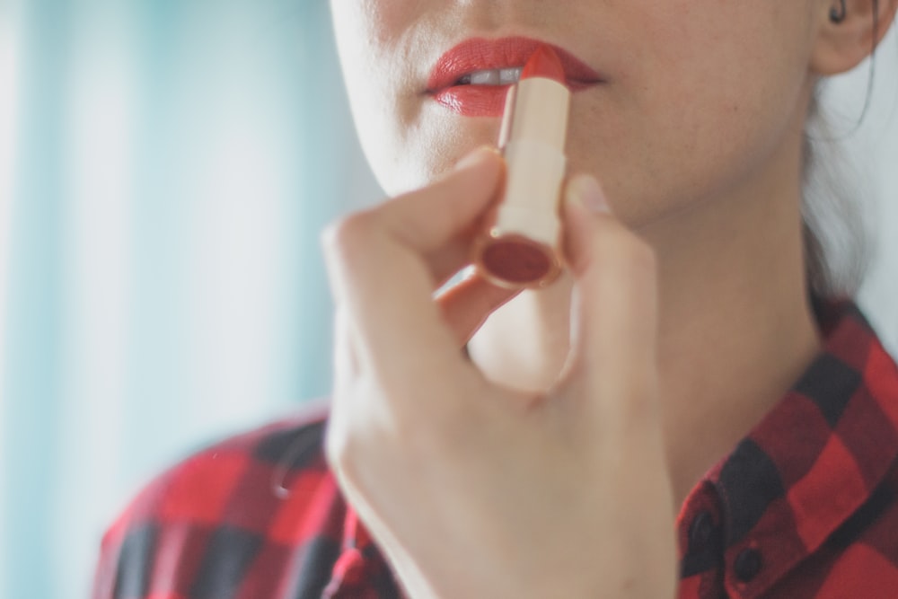 woman in red and black plaid shirt holding lipstick