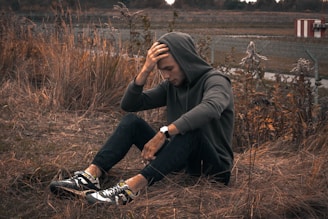 man in black jacket and black pants sitting on brown grass field during daytime