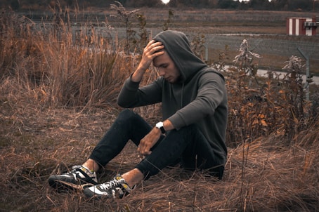 man in black jacket and black pants sitting on brown grass field during daytime