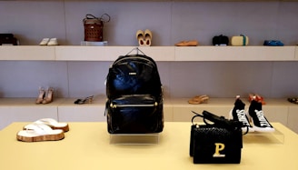 A sleek black and pink-themed display of elegant women's handbags, shoes, and watches arranged stylishly.
