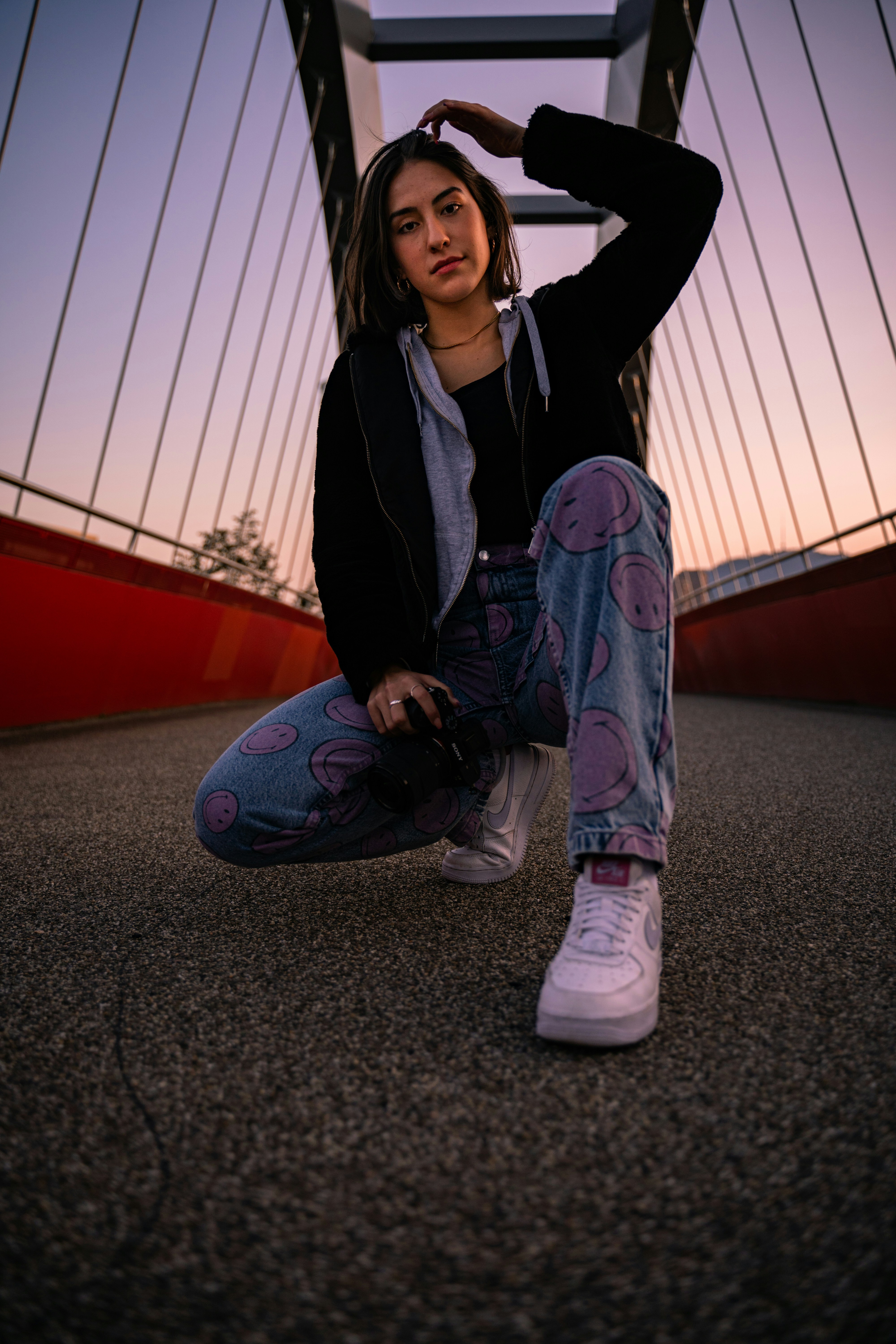 Wanita dengan jaket hitam dan jeans denim biru duduk di lantai beton abu-abu