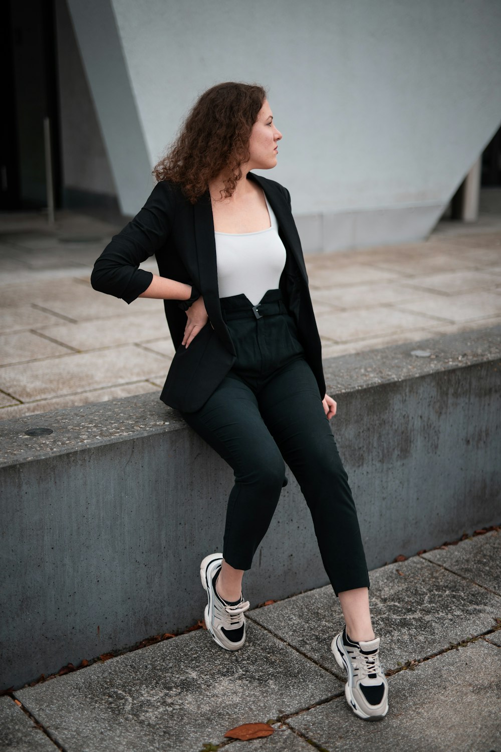 woman in black blazer and black pants sitting on concrete wall during daytime