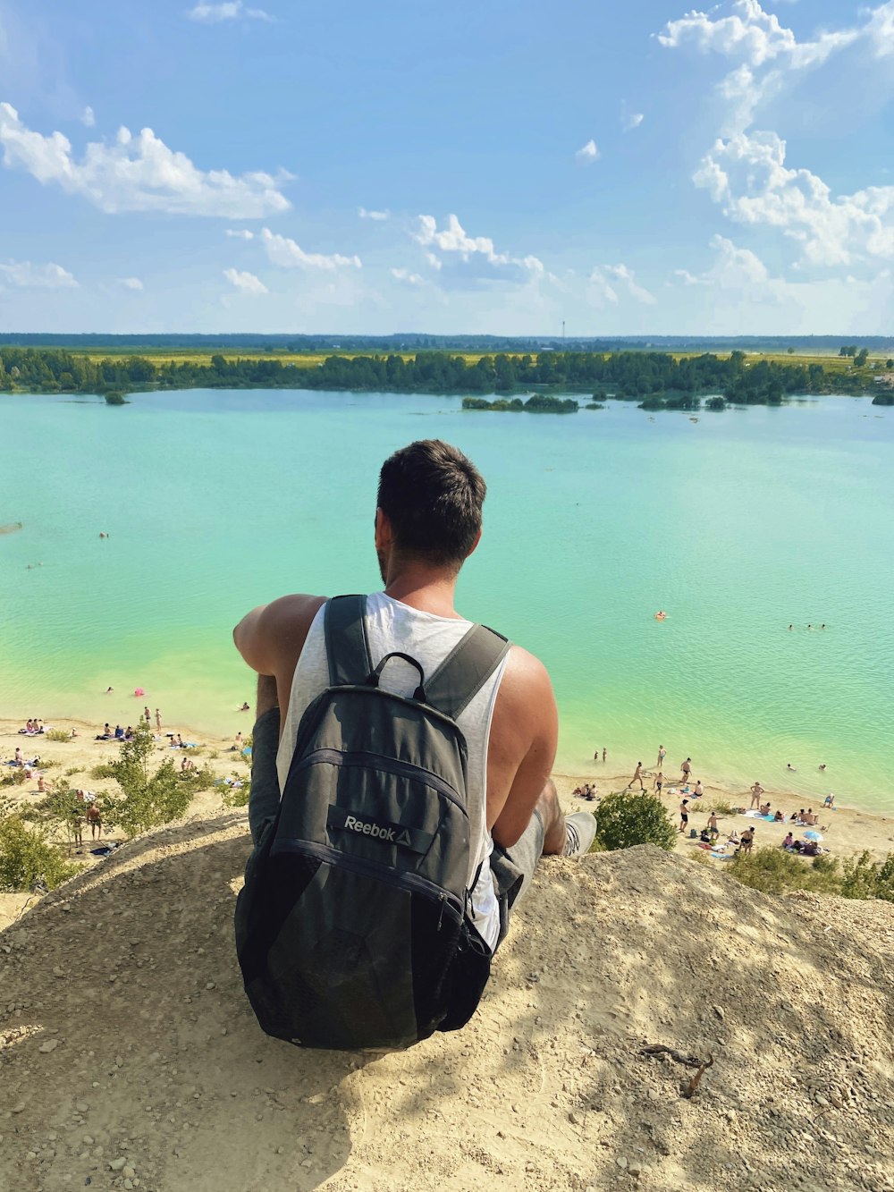 man in black and gray tank top sitting on rock looking at body of water during