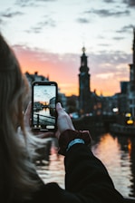 person holding black smartphone taking photo of city buildings during sunset