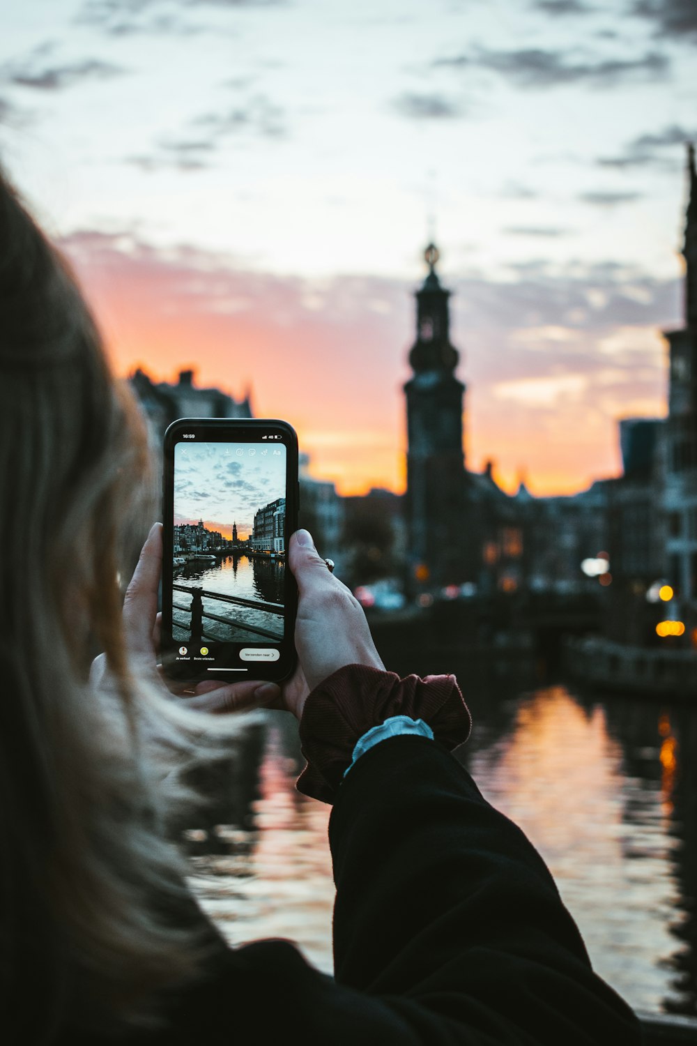person holding black smartphone taking photo of city buildings during sunset