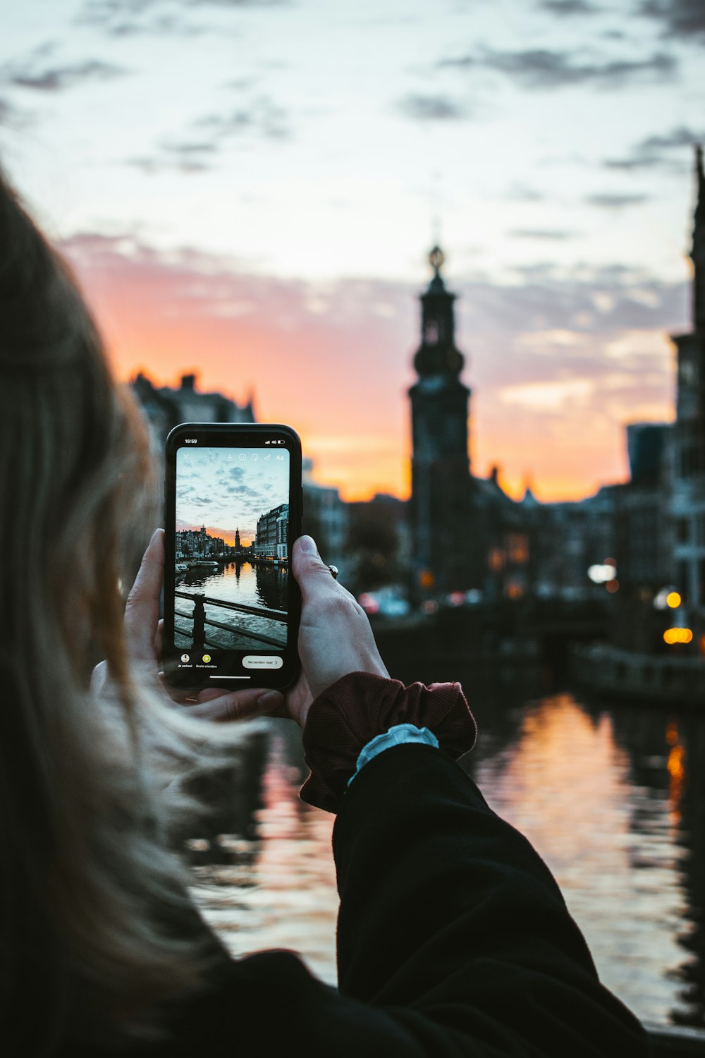 pessoa segurando smartphone preto tirando foto de edifícios da cidade durante o pôr do sol