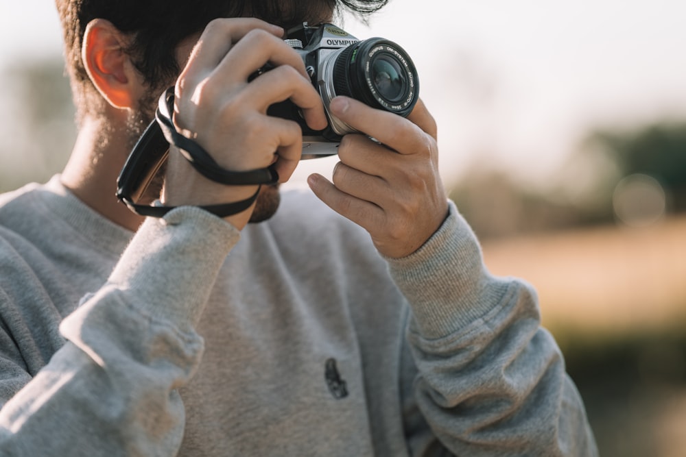 Frau in grauem Pullover mit schwarzer DSLR-Kamera