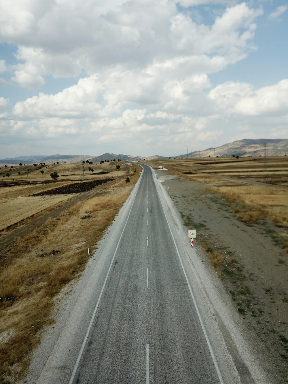 gray asphalt road between brown field under white cloudy sky during daytime