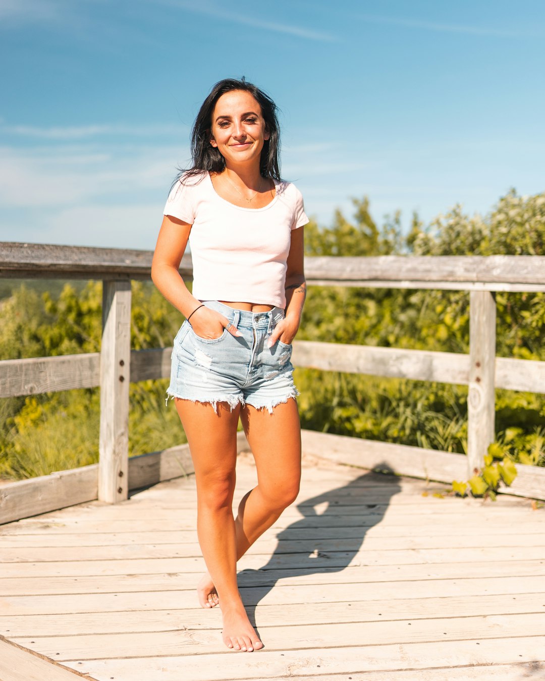 woman in white crew neck t-shirt and blue denim shorts standing on brown wooden dock