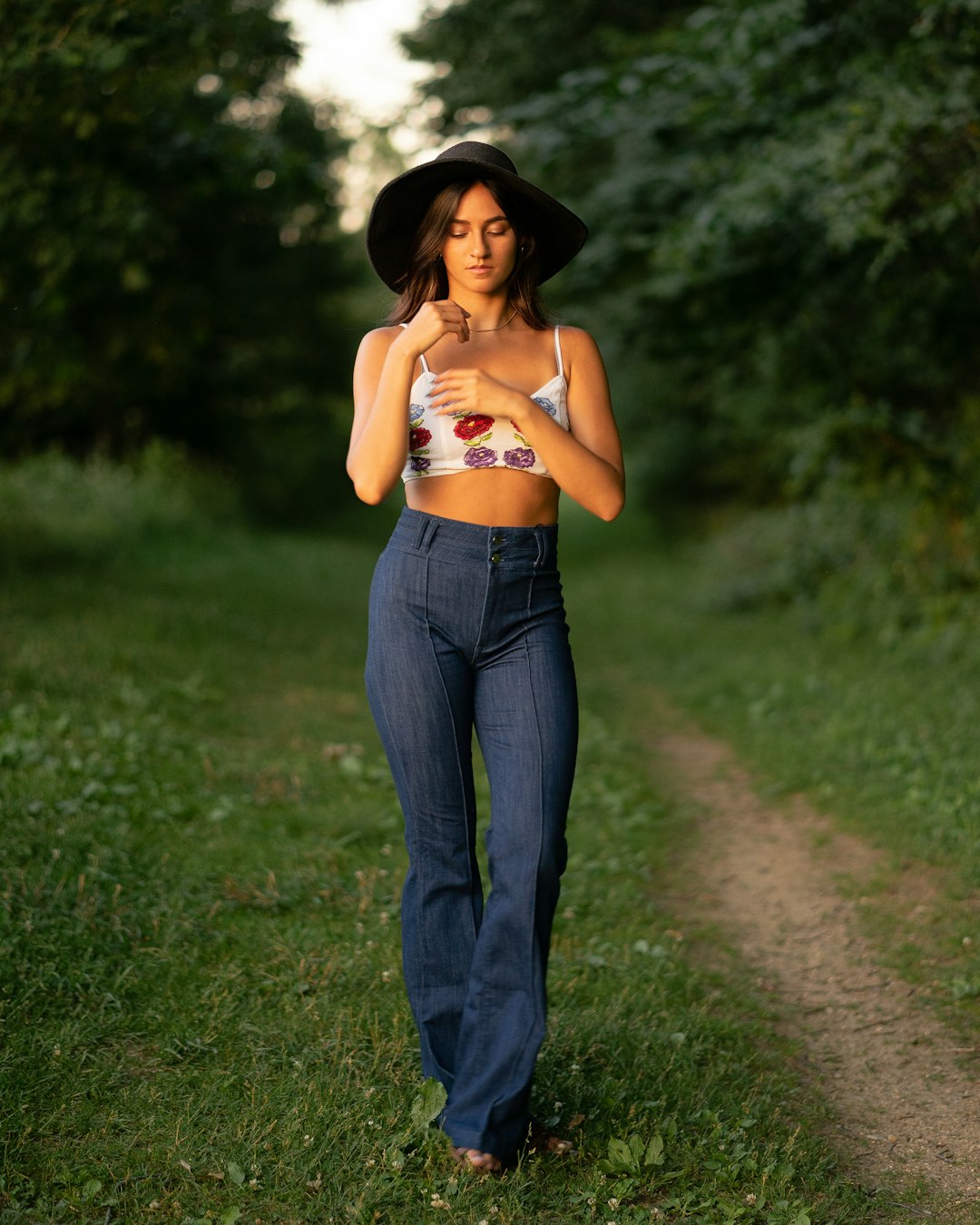 woman in orange crop top and blue denim jeans wearing black hat standing on green grass