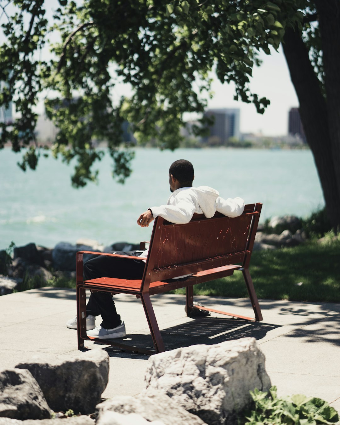 man in white shirt sitting on brown wooden chair near body of water during daytime