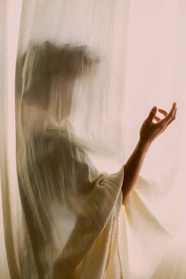 A silhouette of a woman wrapped in silky fabric illuminated by soft golden light, evoking elegance and mystery.