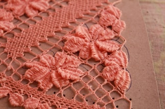 Detailed crochet work in pink, showcasing intricate floral patterns on a grid of loops. The flowers are prominently featured in a dense arrangement, highlighting craftsmanship and texture against a neutral background.