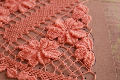 Detailed crochet work in pink, showcasing intricate floral patterns on a grid of loops. The flowers are prominently featured in a dense arrangement, highlighting craftsmanship and texture against a neutral background.