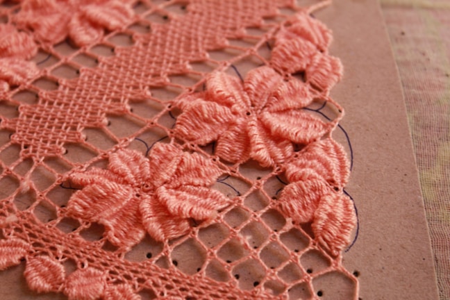 Close-up of a delicate pink crochet flower on a soft fabric background.