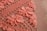 Detailed crochet work in pink, showcasing intricate floral patterns on a grid of loops. The flowers are prominently featured in a dense arrangement, highlighting craftsmanship and texture against a neutral background.