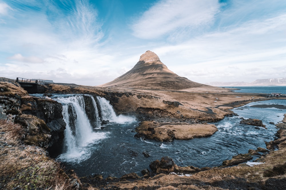 waterfalls near brown mountain under blue sky during daytime