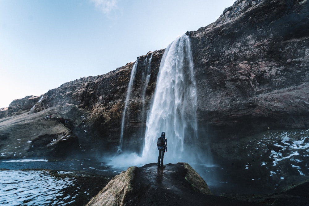 man standing on rock near waterfalls during daytime