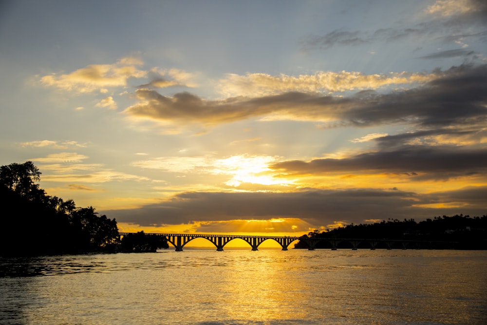 silhueta da ponte sobre o corpo de água durante o pôr do sol