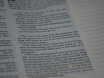 Text from a religious or spiritual book is visible on an open page. The words are printed in a formal font, and the page is filled with neatly organized columns of text. The focus is on a specific passage that appears to be discussing blessings and protection.