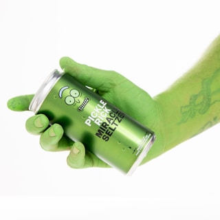 A hand painted green is holding a green can labeled 'Pickle Rick Miracle Seltzer.' The design on the can includes a cartoon face with a quirky expression.