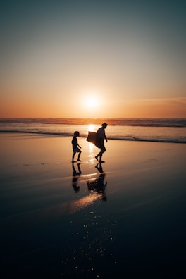 A sunset silhouette of the father and daughter walking side by side along a beach.