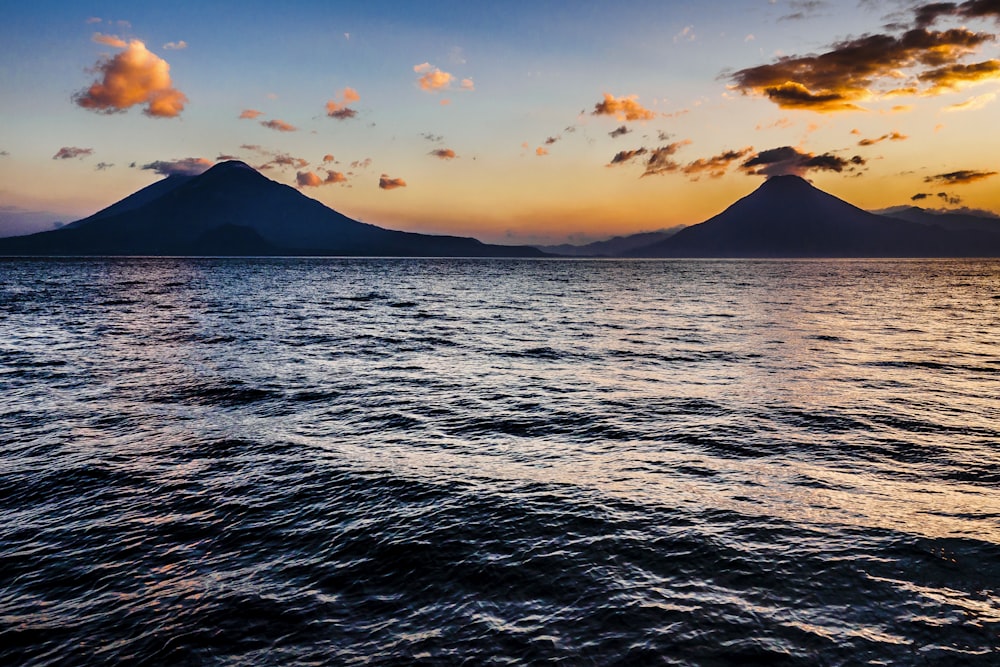 body of water near mountain during sunset