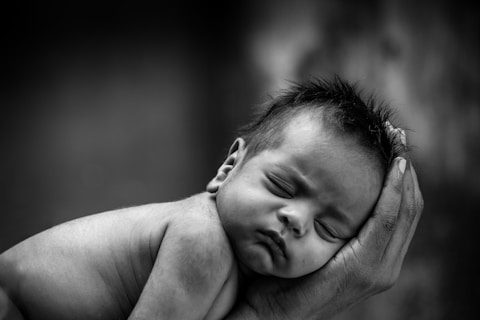 Black and white frowning baby asleep with face in a hand 