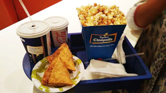 A tempting tray filled with golden popcorn, nachos topped with melted cheese, and a cold soda, ready for delivery.