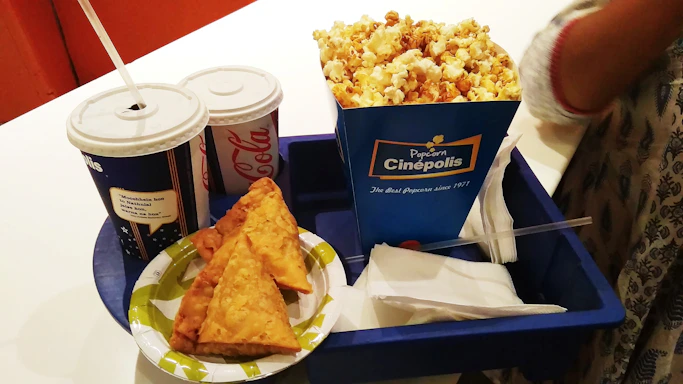 A tempting tray filled with golden popcorn, nachos topped with melted cheese, and a cold soda, ready for delivery.