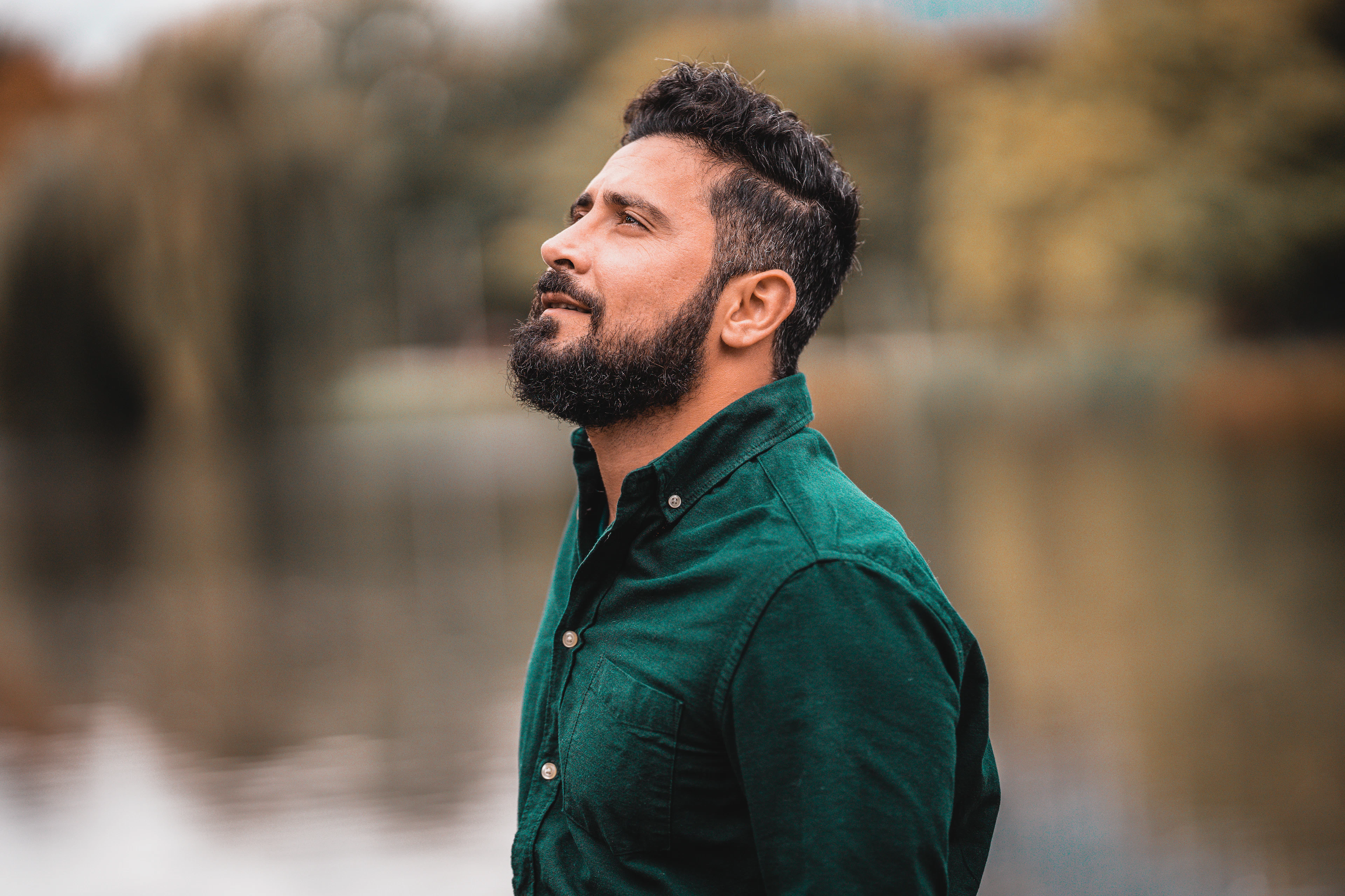 Homem de barba com camisa social verde musgo à beira de um lago