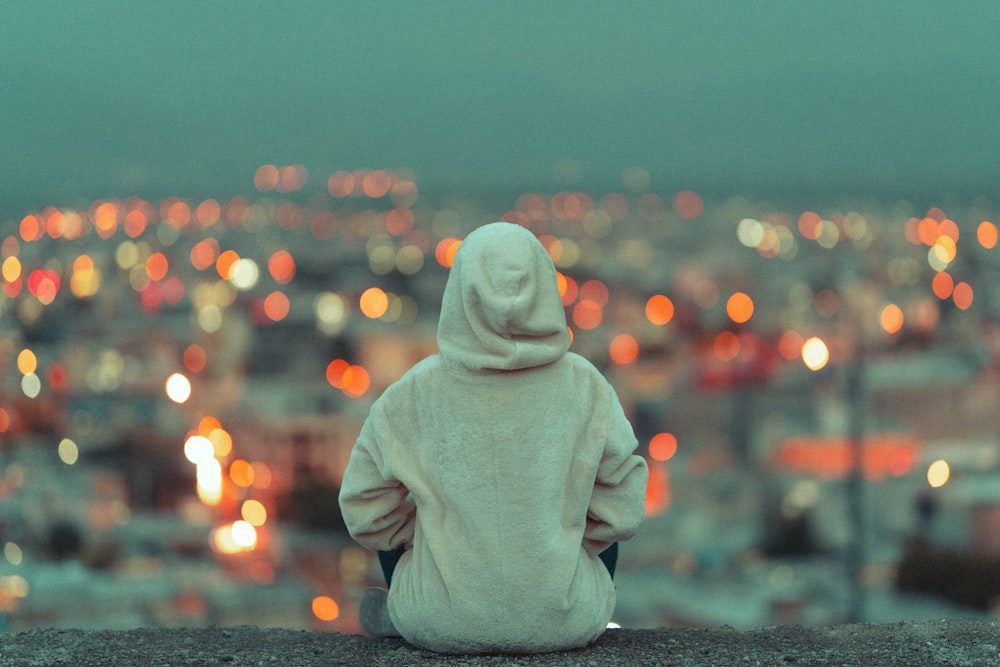 person in white hoodie sitting on gray concrete floor during daytime