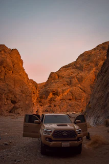 A rugged van parked on a rocky outcrop overlooking a vast desert at golden hour, with warm sunlight casting long shadows.